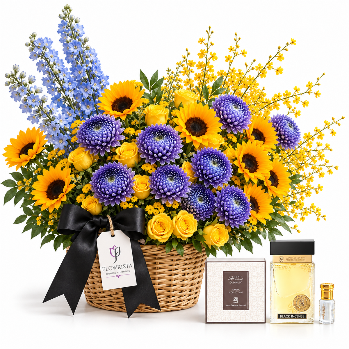 A floral gift basket arrangement in a woven basket with a black ribbon bow and tag reading FLOWRISTA, filled with yellow sunflowers, purple chrysanthemums, blue delphiniums, and yellow roses, shown with a boxed perfume and a small bottle on a white background.