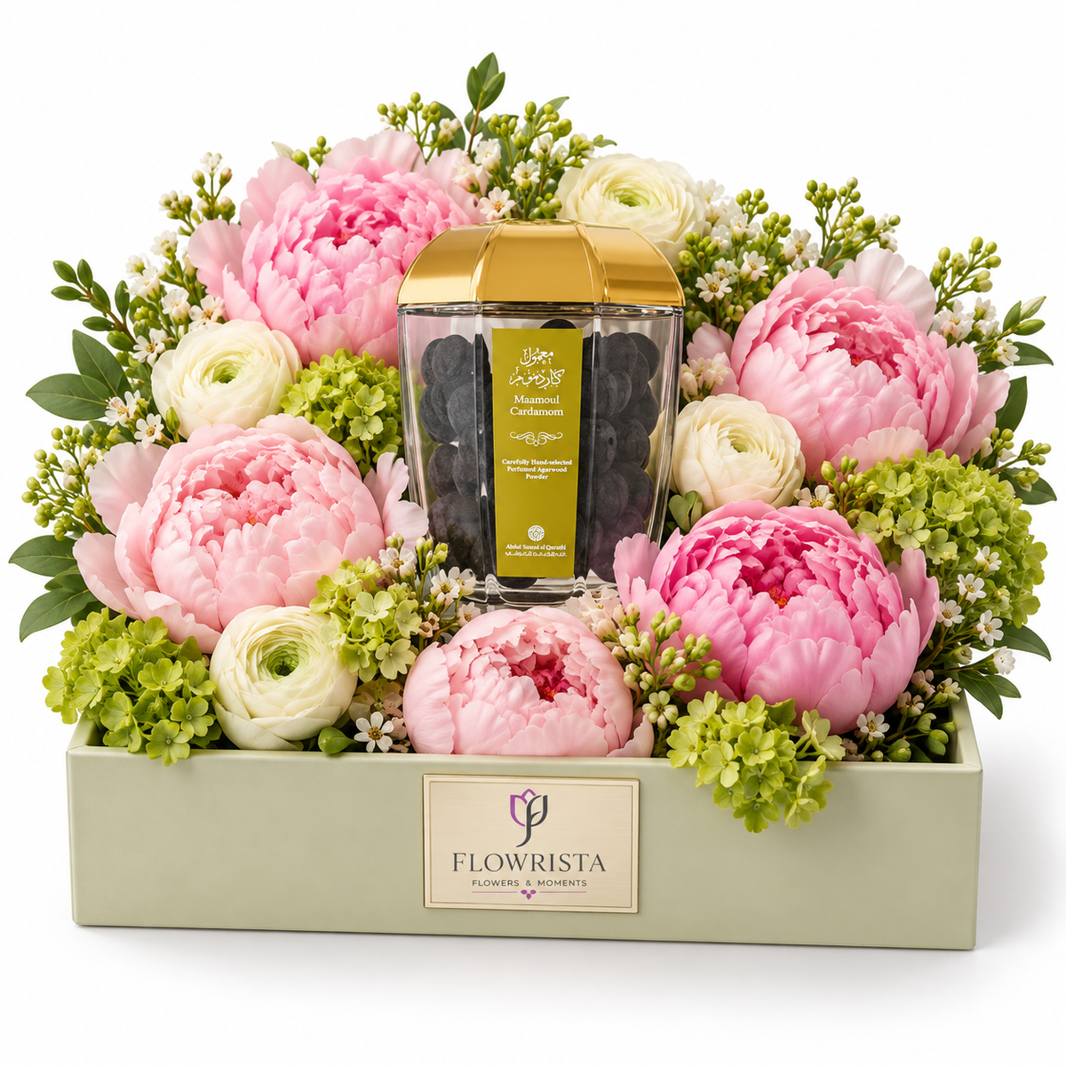 A floral gift arrangement in a pale sage green box with a central glass jar of dark chocolate and a gold lid, surrounded by large pink peonies, white ranunculus, and green hydrangeas. The front of the box reads FLOWRISTA.