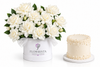 A white floral box filled with white peonies and green leaves, next to a small round cream-colored cake with decorative drizzle, on a clean white background. The box is branded FLOWRISTA.