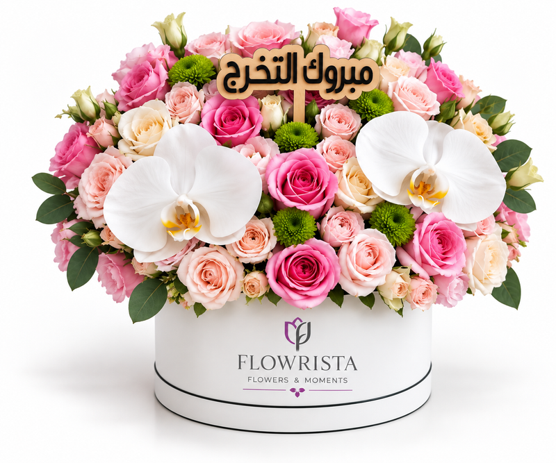 A large, vibrant floral arrangement in a round white box from Flowrista, featuring pink and peach roses, white orchids, green accents, and a wooden Arabic name plaque in the center, set against a plain white background.