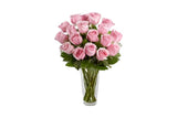A bouquet of 15 pink roses in a clear glass vase with green stems, set against a plain white background.