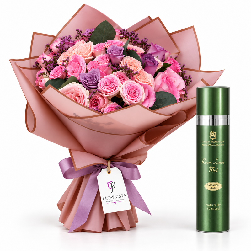 A bouquet of pink and purple roses wrapped in pink paper with a purple ribbon and a tag reading FLOWBISTA, shown next to a green cylindrical bottle labeled Roseine Lotion Mist on a white background.