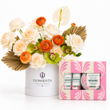 A floral gift arrangement in a white round box from Flowrista, featuring cream and orange flowers with green leaves, displayed next to a pink and cream 'The Body Shop' British Rose body butter and bath bomb gift set on a white background.