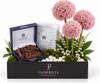 A luxury gift set from Flowrista featuring three pink allium-style flowers, a box of dark brown chocolate bark, and a white floral box inside a black presentation container with the Flowrista logo.