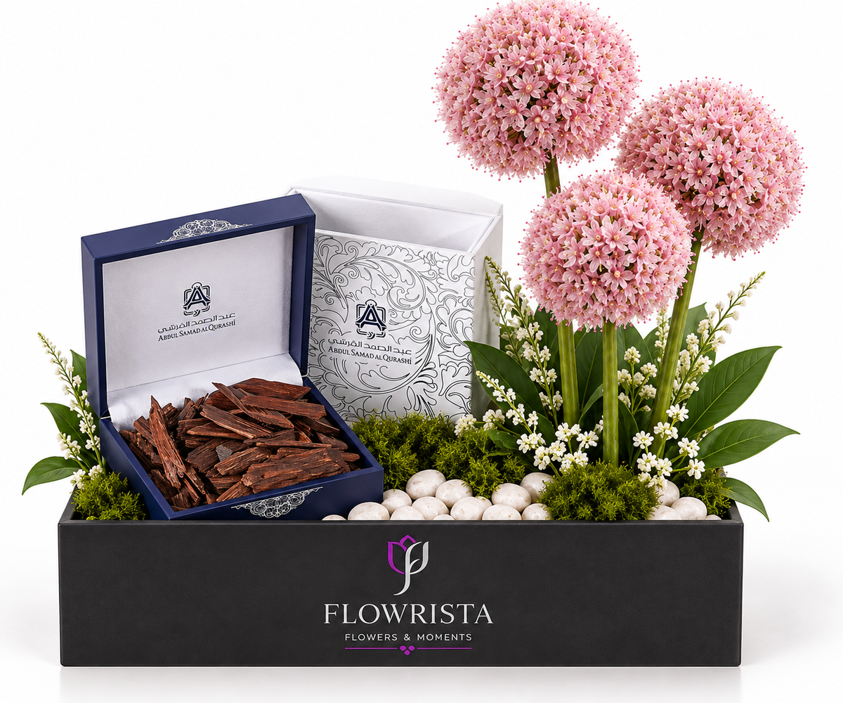 A luxury gift set from Flowrista featuring three pink allium-style flowers, a box of dark brown chocolate bark, and a white floral box inside a black presentation container with the Flowrista logo.
