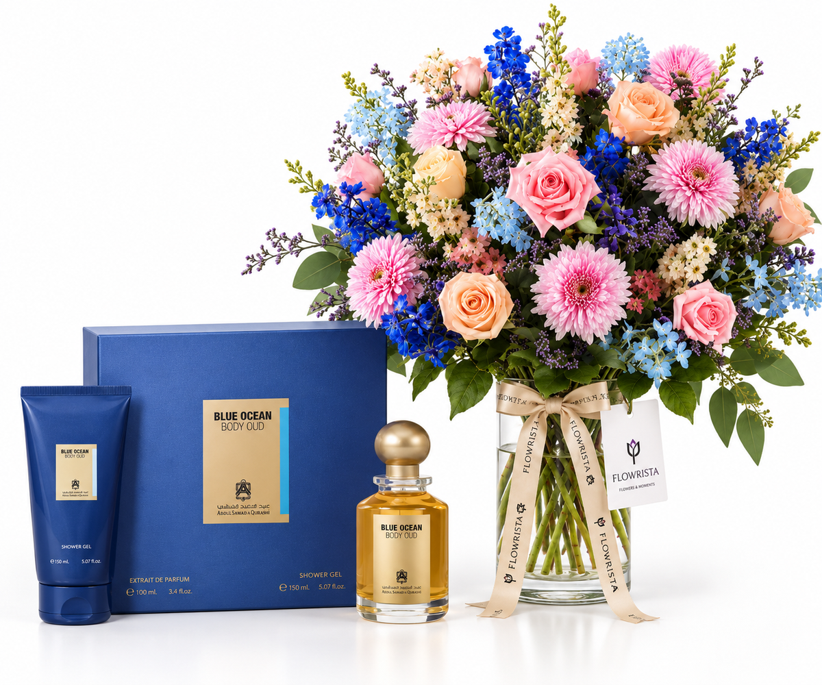A luxury gift set featuring a blue floral arrangement in a glass vase with a ribbon, a blue gift box, a blue body wash tube, and a blue-and-gold perfume bottle on a white background.