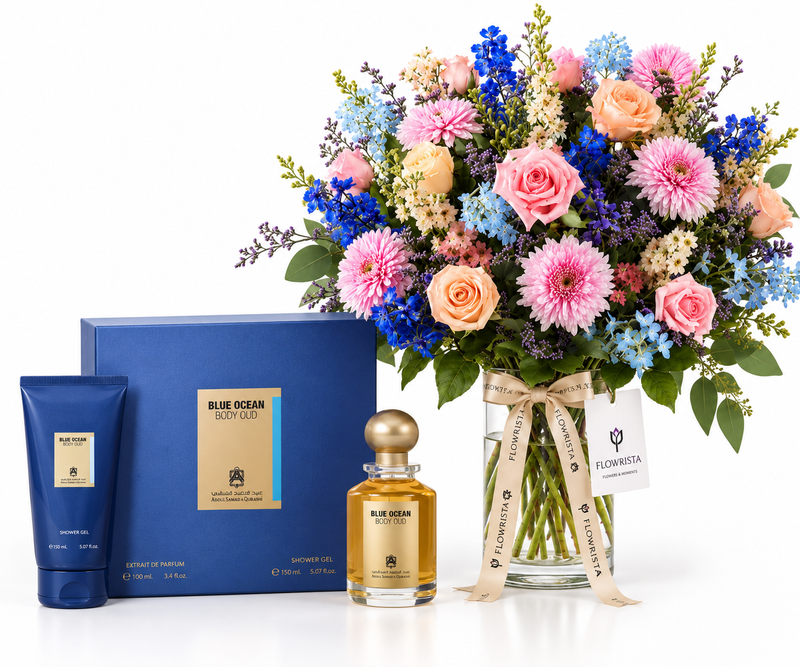 A luxury gift set featuring a blue floral arrangement in a glass vase with a ribbon, a blue gift box, a blue body wash tube, and a blue-and-gold perfume bottle on a white background.