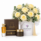 A gift set featuring a bottle of Qurashi Blend perfume, a jar of the same fragrance, a brown branded box, a white flower box labeled Flowrista with pale yellow roses, and a gold tassel, arranged on a clean white background.