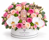 A luxury floral gift arrangement featuring a pink Chanel No. 5 perfume bottle nestled in a vibrant bouquet of pink and peach roses, white orchids, and green foliage, presented in a white round box branded FLOWWRISTA.