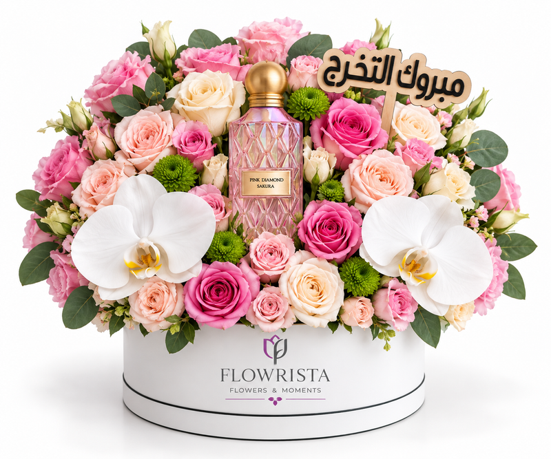 A luxury floral gift arrangement featuring a pink Chanel No. 5 perfume bottle nestled in a vibrant bouquet of pink and peach roses, white orchids, and green foliage, presented in a white round box branded FLOWWRISTA.