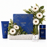 A luxury gift set for men featuring a blue Safari Blue cologne set, including a blue tube, a blue box, and a blue bottle, beautifully arranged with white gerbera daisies in a green vase and white baby's breath on a bed of white decorative beads. A 'FLOWRISTA' gift tag is attached to the front.