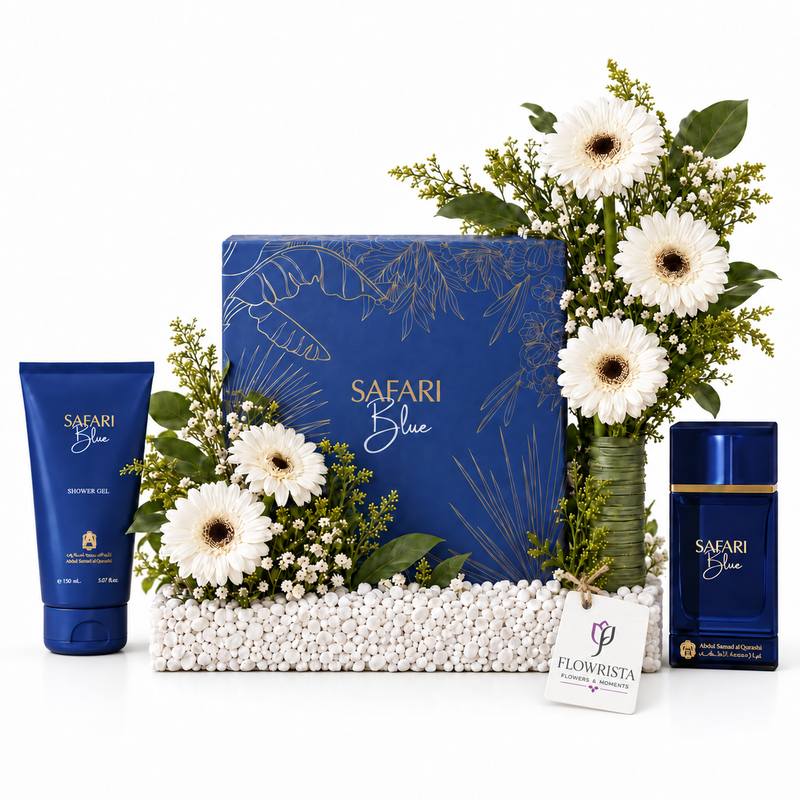 A luxury gift set for men featuring a blue Safari Blue cologne set, including a blue tube, a blue box, and a blue bottle, beautifully arranged with white gerbera daisies in a green vase and white baby's breath on a bed of white decorative beads. A 'FLOWRISTA' gift tag is attached to the front.
