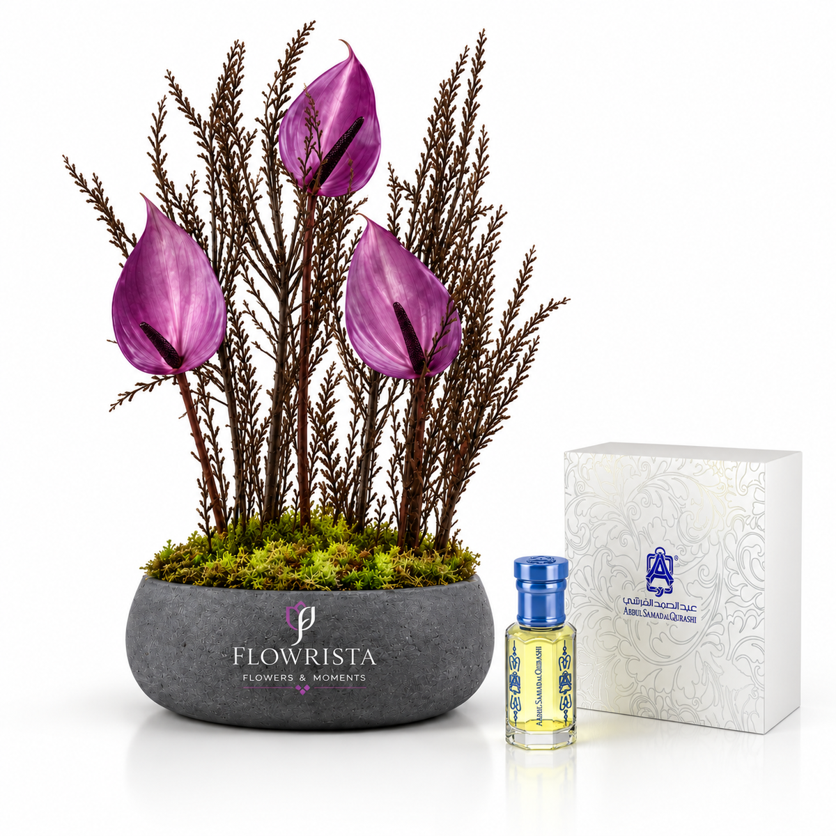 A floral arrangement in a round gray stone pot with purple calla lilies and dark brown feathery stems, shown beside a small perfume bottle and a white branded box on a clean white background. The pot is labeled FLOWRISTA.