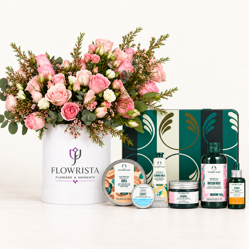 A curated gift set featuring a large pink and white flower arrangement in a white Flowerista box, alongside a green patterned gift tin and several small skincare and bath products on a clean white background.