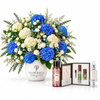 A large floral arrangement in a white vase labeled FLOWWRISTA, featuring vivid blue and white flowers with green foliage, displayed beside a small gift set containing a red patterned bottle, a boxed set with green and silver items, and a clear perfume bottle on a white background.