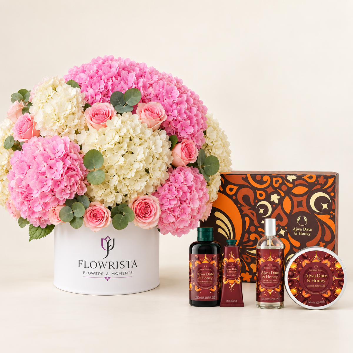 A floral gift set from Flowrista featuring a large bouquet of pink and cream hydrangeas and roses in a white pot, alongside a matching 'Apna Dast & Honey' apothecary set including a box, lotion, hand cream, and a tin.