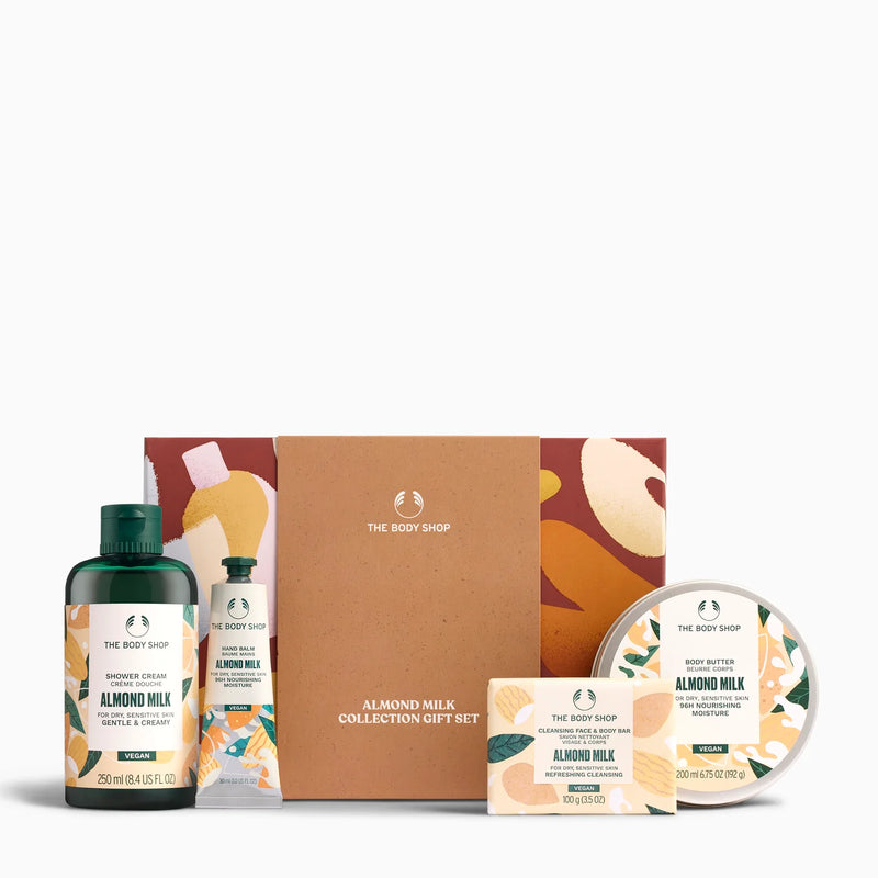 The Body Shop Almond Milk Collection Gift Set featuring a brown cardboard gift box, a dark green shower gel bottle, a hand and foot wash bottle, a soap bar, and a round body butter tin, all arranged on a white background.