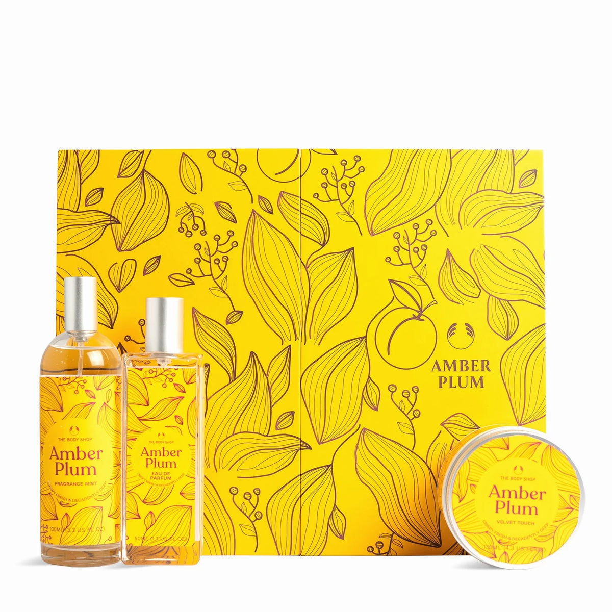 A gift set for 'Amber Plum' featuring two amber-colored bottles with silver caps, a round tin, and a large square box, all decorated with a yellow and orange floral pattern.
