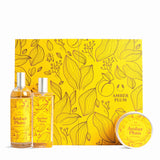 A gift set for 'Amber Plum' featuring two amber-colored bottles with silver caps, a round tin, and a large square box, all decorated with a yellow and orange floral pattern.