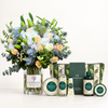 A curated gift set featuring a large floral arrangement in a glass vase labeled FLOWWRISTA, alongside The Body Shop bath and body products including a white tea & elderflower shower foam bottle, hand cream tube, body wash bottle, and body butter tin, arranged on a white surface against a clean white background.