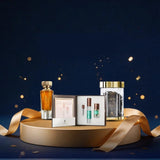 A luxury gift set displayed on a round gold pedestal against a dark navy blue background with gold bokeh and ribbon accents. The set includes a tall amber perfume bottle, a small vial, a green serum bottle, and a clear jar with a gold lid, arranged with a gold ribbon.