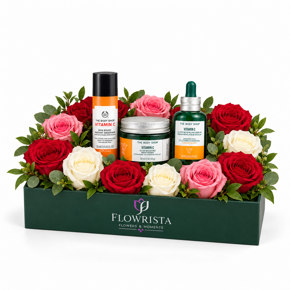A curated gift basket by Flowrista featuring skincare products from The Body Shop and Vitamin C, beautifully arranged in a dark green box with red, pink, and white roses and green foliage, set against a plain white background.
