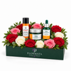 A curated gift basket by Flowrista featuring skincare products from The Body Shop and Vitamin C, beautifully arranged in a dark green box with red, pink, and white roses and green foliage, set against a plain white background.