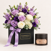 A luxury gift set featuring a black box of 'Flowrista' flowers and moments with a purple satin ribbon, next to a jar of 'Sapna' French Grape Seed Scrub, set against a clean off-white background.