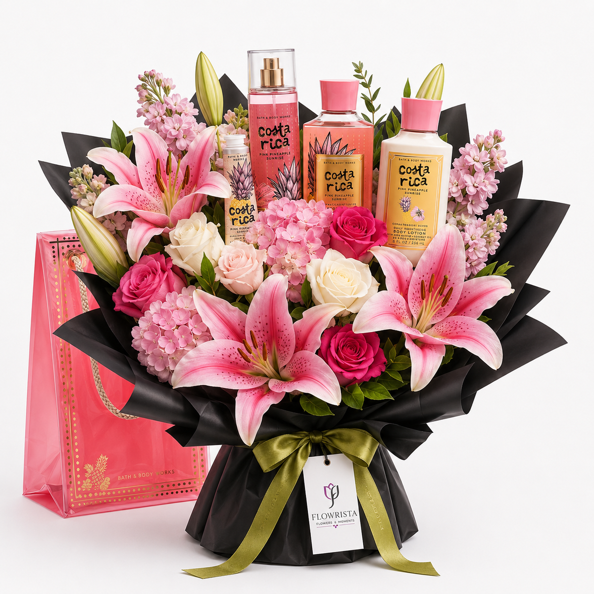 A floral gift bouquet with pink lilies, pink and white roses, hydrangeas, green buds, and three Costa Rica-themed bottles arranged behind the flowers. A pink gift bag and black wrapped bouquet base with a green ribbon are visible on a clean white background.