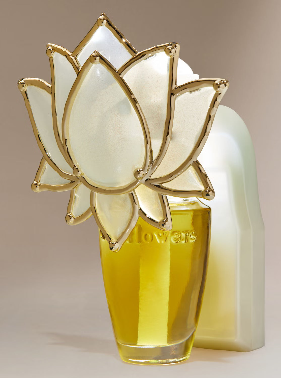 A perfume bottle with a translucent white lotus flower cap outlined in gold, filled with yellow liquid, standing in front of a white bottle on a beige background.