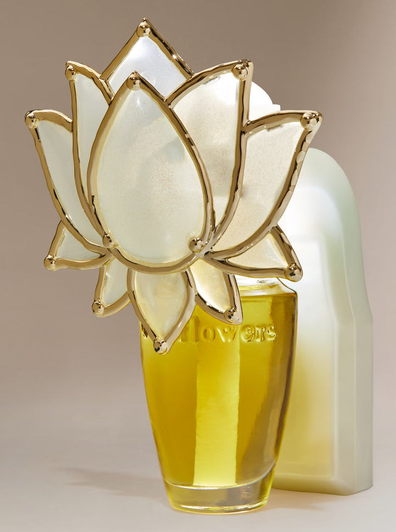 A perfume bottle with a translucent white lotus flower cap outlined in gold, filled with yellow liquid, standing in front of a white bottle on a beige background.