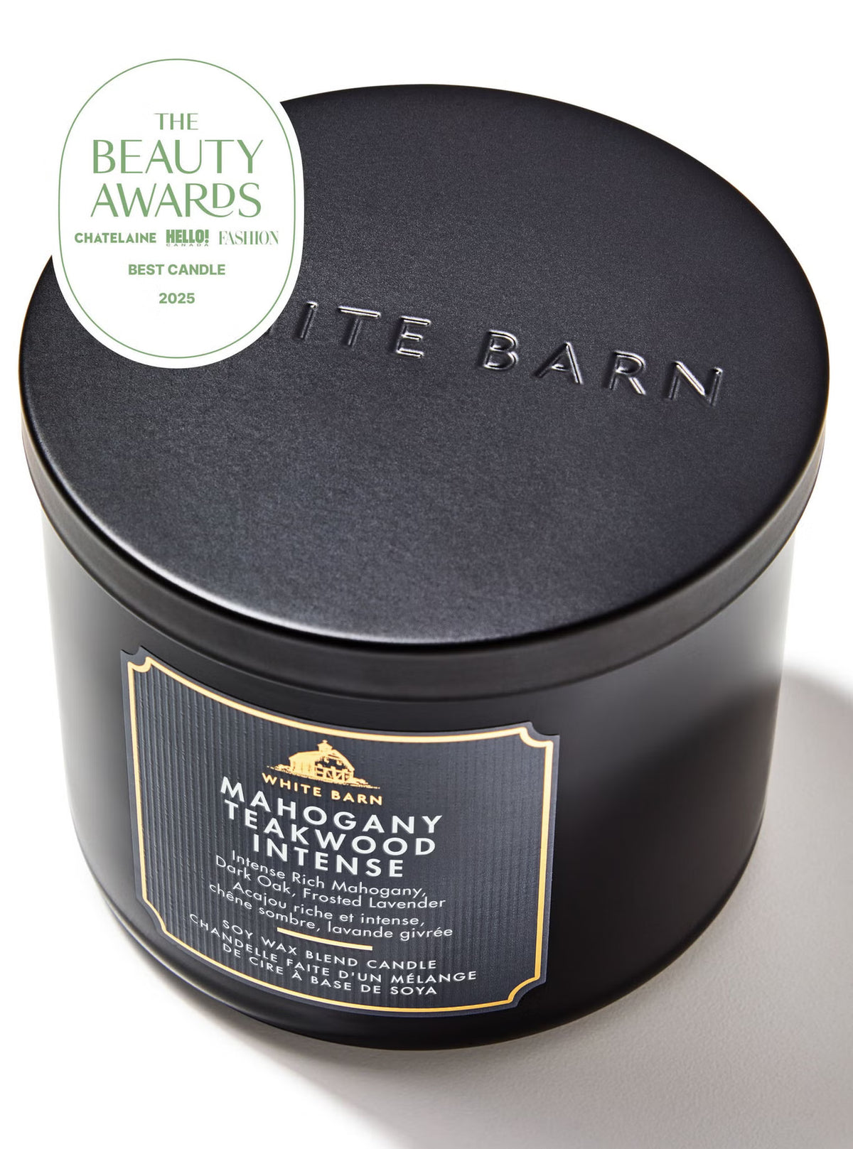 A matte black cylindrical tin candle from White Barn, featuring a gold and black label on the front and 'BARN' embossed on the lid. A white circular 'The Beauty Awards 2023 Best Candle' badge is overlaid in the top-left corner.