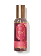 A bottle of Heirloom Rose Aromatherapy Essential Oil Perfume Mist by Bath & Body Works, featuring a metallic gold cap and a deep rose-pink label, set against a clean white background with a soft shadow.