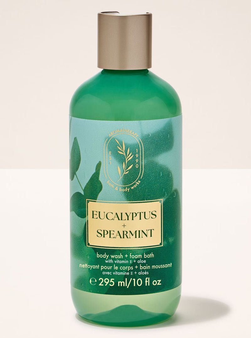 A bottle of Bath Body Works Eucalyptus + Spearmint body wash and foam bath in a translucent green bottle with a metallic gold cap, set against a plain off-white background.