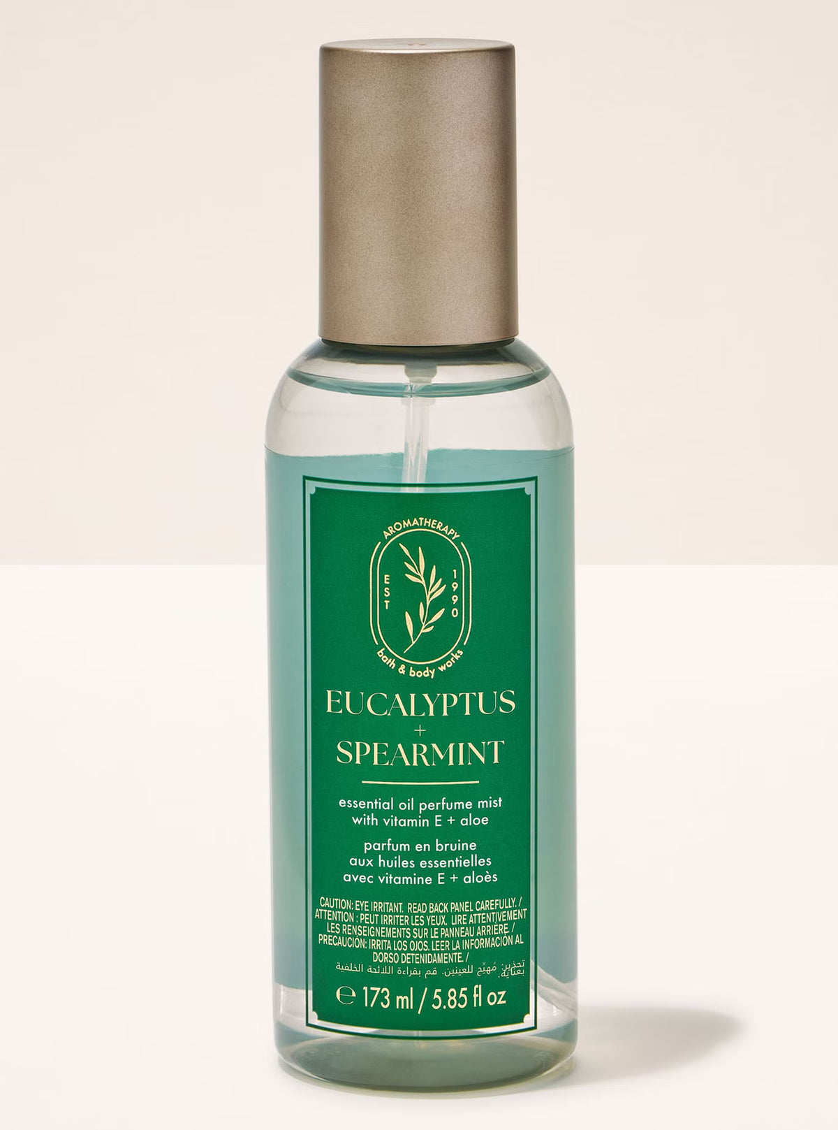 A bottle of Eucalyptus Spearmint essential oil perfume mist by The Scent Shop. The bottle is made of clear plastic showing a light teal liquid inside, with a green label and a metallic silver cap, set against a plain off-white background.