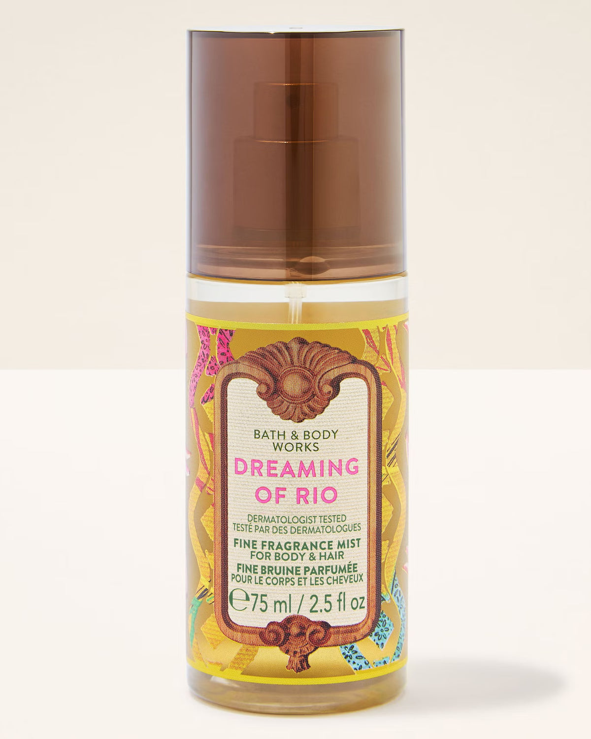 A bottle of Bath & Body Works Dreaming of Rio Fine Fragrance Mist for body and hair, featuring a translucent brown cap and a colorful yellow label with pink and brown accents, set against a plain off-white background.