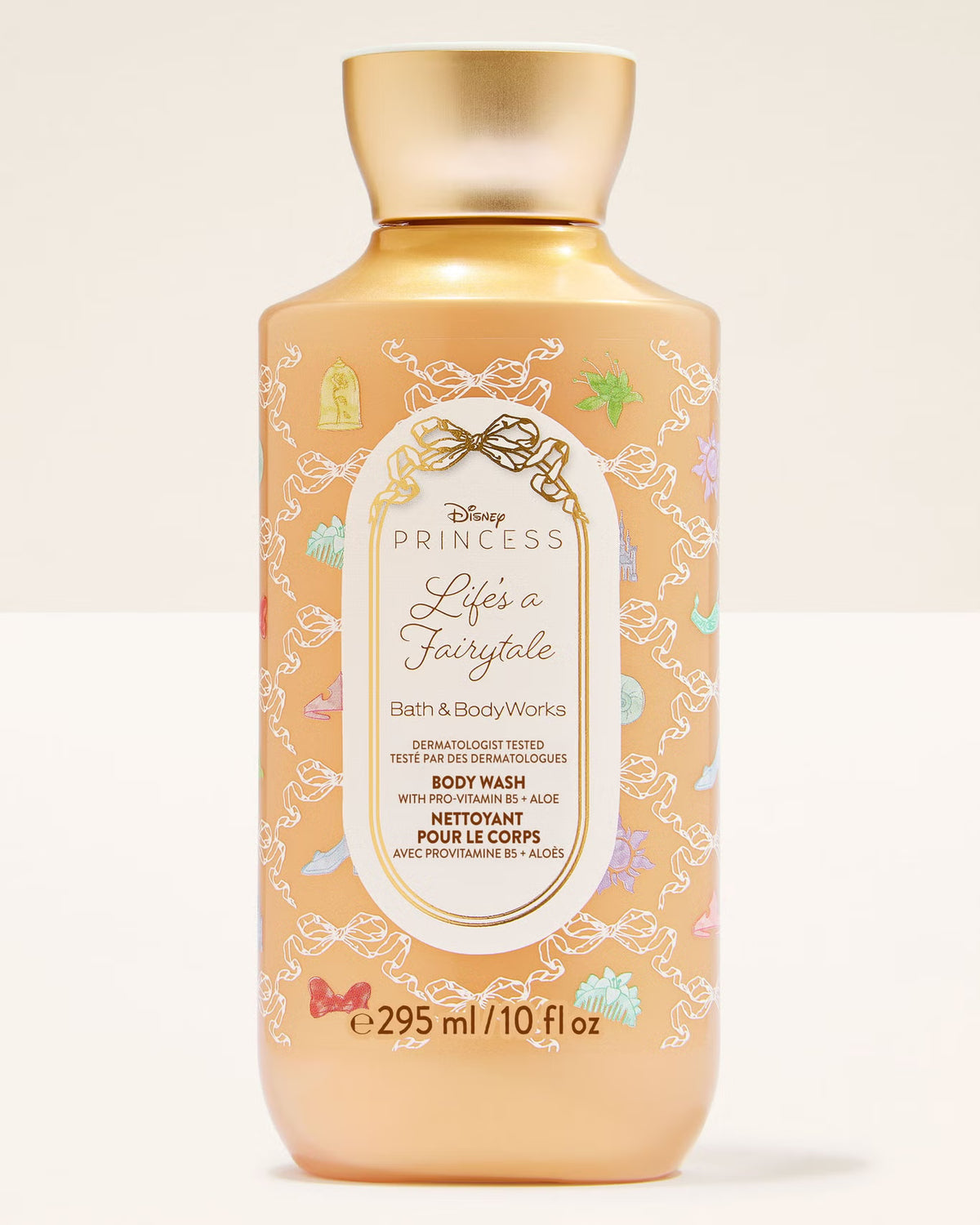 Disney Princess Life is a Fairytale Body Wash in a 10 fl oz bottle. The bottle is a warm peach-beige color with a metallic gold cap and features white lace illustrations and multicolored fairy accents on the label.