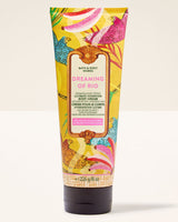 A squeeze tube of Bath & Body Works Dreaming of Rio Ultimate Hydration Body Cream, featuring a vibrant yellow background with colorful tropical bird and floral illustrations, set against a plain off-white background.