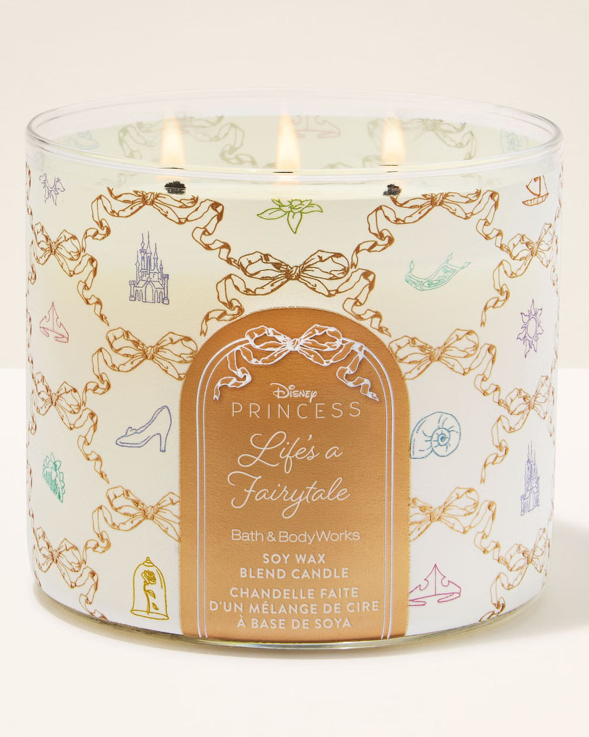 A three-wick Disney Princess 'Life's a Fairytale' soy wax blend candle in a clear glass jar with a white label decorated with gold chain motifs and small pastel fairy tale illustrations. The label features the Disney Princess logo and product details.