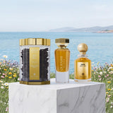 Three fragrance products from QuraSh Blend are displayed on a white marble pedestal with a scenic beach and wildflower background. The set includes a clear hexagonal tin filled with dark incense sticks, a tall rectangular glass bottle with amber liquid and gold detailing, and a round glass bottle with amber liquid and a gold spherical cap.