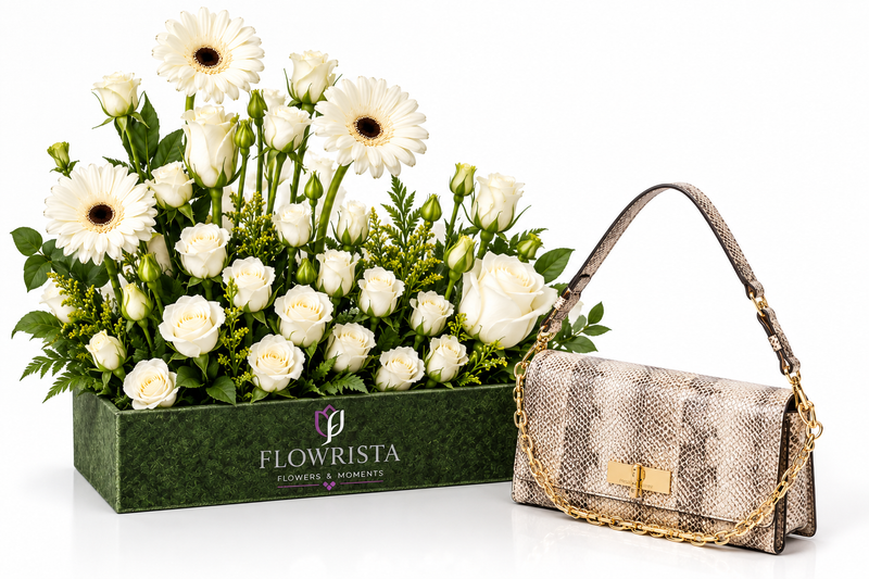 A luxury gift set featuring a green rectangular box of white flowers, including daisies and roses, next to a beige snakeskin-patterned shoulder bag with gold chain and lock details. The box is branded 'FLOWRISTA'.