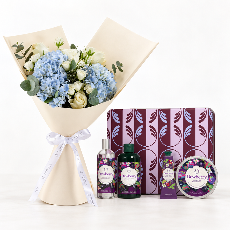 A floral gift set featuring a bouquet of blue hydrangeas, white roses, and green eucalyptus wrapped in beige paper with a white ribbon, alongside a purple patterned box and matching Desuberry body care products including a bottle, tube, and tin.