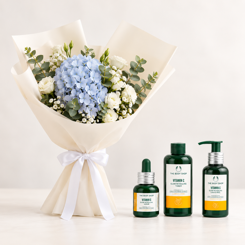 A floral bouquet wrapped in cream paper with a white ribbon bow, alongside three bottles from The Body Shop Vitamin C skincare set on a clean white surface against a light beige background.