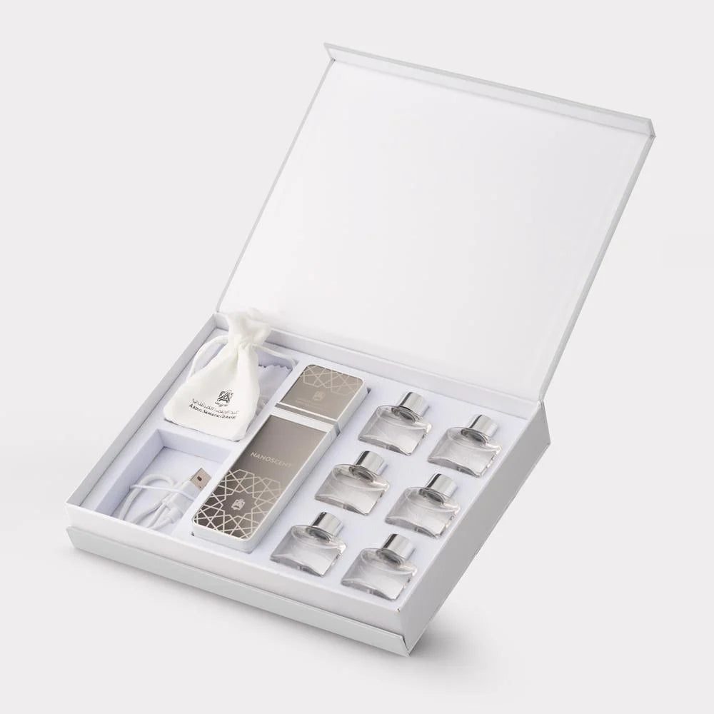 An open white gift box containing a skincare or fragrance set, including a rectangular silver-toned bottle, several small clear glass bottles with silver caps, a white drawstring pouch, and a white cable, photographed on a clean white background.