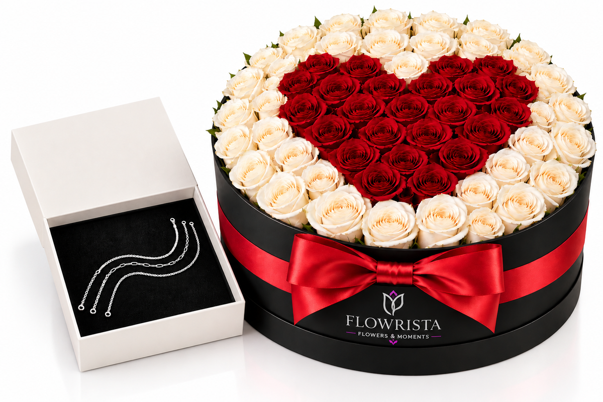 A round black gift box filled with roses arranged in a heart shape of deep red roses, surrounded by cream-white roses. A red ribbon bow is tied around the box, and the brand name 'FLOWRISTA' is visible on the front.