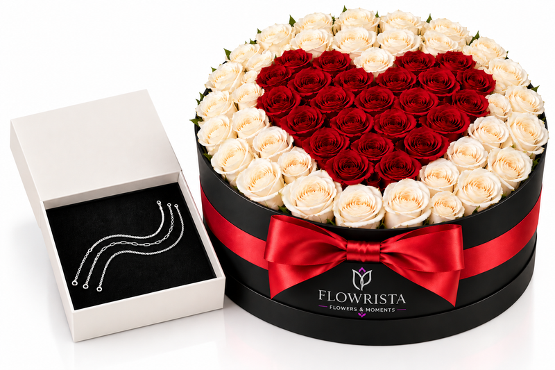 A round black gift box filled with roses arranged in a heart shape of deep red roses, surrounded by cream-white roses. A red ribbon bow is tied around the box, and the brand name 'FLOWRISTA' is visible on the front.