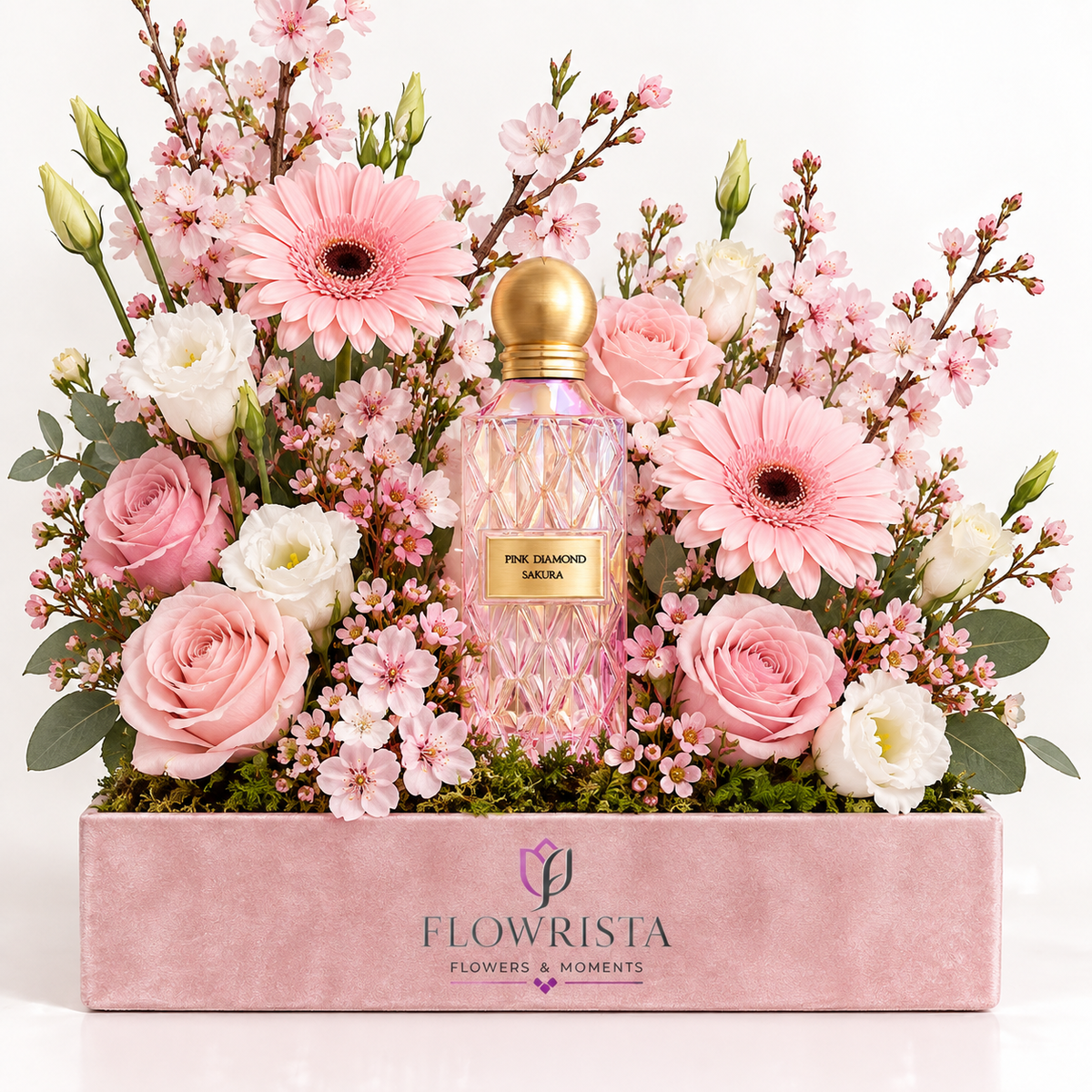 A pink diamond-cut perfume bottle with a gold cap nestled in a large floral arrangement of pink roses, pink gerbera daisies, white lisianthus, and pink blossoms, presented in a pink box branded FLOWRISTA.