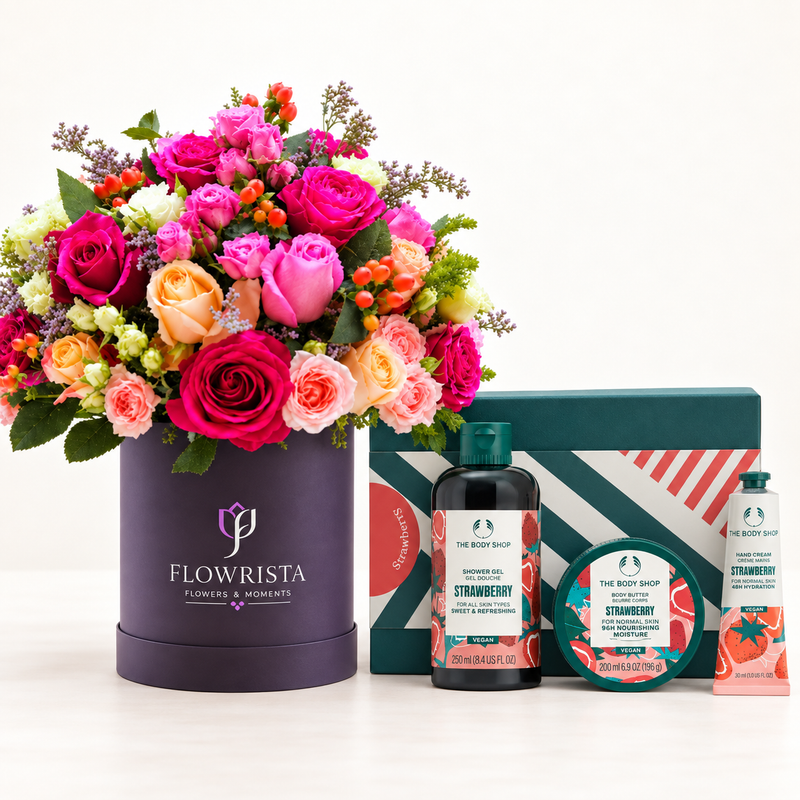A curated gift set featuring a large, vibrant flower arrangement in a dark purple cylindrical box labeled 'FLOWRISTA', alongside The Body Shop strawberry-themed bath and body products including a bottle, a round tin, and a tube, set against a clean white background.