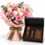 A floral gift bouquet wrapped in pink paper with a green ribbon bow, displayed beside an open black gift box containing two amber bottles and a small card labeled Vintage Tobacco on a white background.