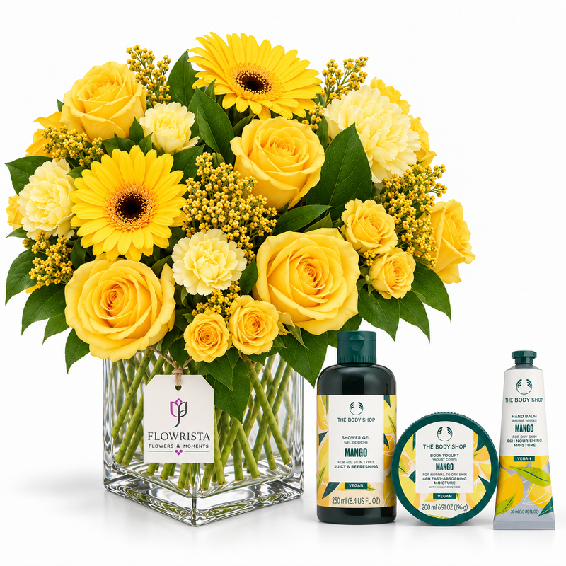 A yellow flower bouquet in a clear square glass vase with a Flowrista tag, alongside three The Body Shop Mango body care items on a white background.